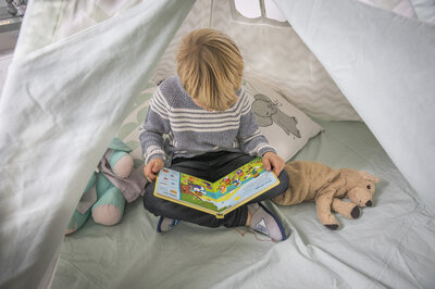 En liten pojke sitter i ett lektält och läser i en bok.