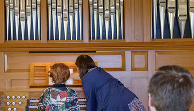 Kvinna pekar på noterna medans ett rödhårigt barn spelar på en orgel.