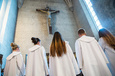 Konfirmander i vita kåpor står framför altare med ett stort Jesus krucifix över.