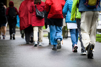 En grupp iklädd regnkläder och ryggsäckar går på en asfaltsväg.