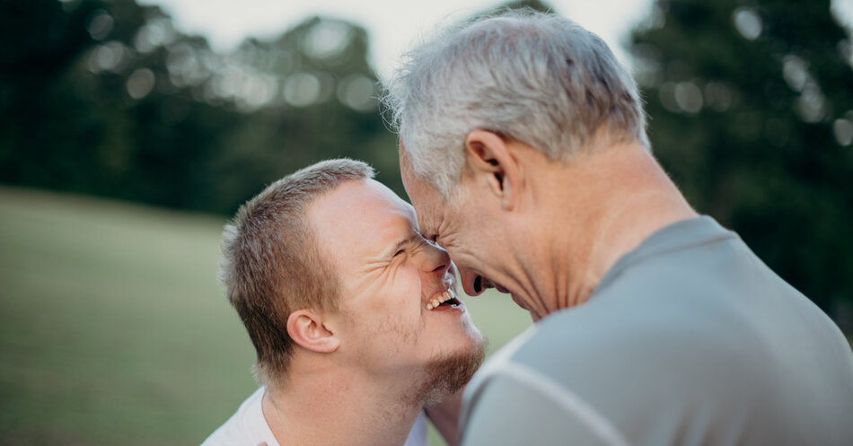 Äldre gråhårig man håller om och skrattar med en yngre man på ett fält. | © Foto: Nathan Anderson, Unsplash