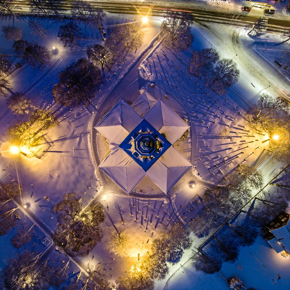 Drönar bild tagen rakt ovanför kyrka visar snötäckt kyrktak samt snötäckt kyrkogård. 