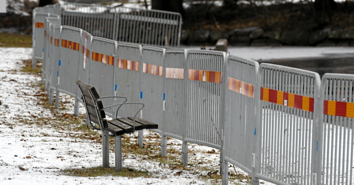 Park med tunt snölager på marken där en bänks utsikt blivit blockerat av ett långt provisoriskt uppsatt staket.