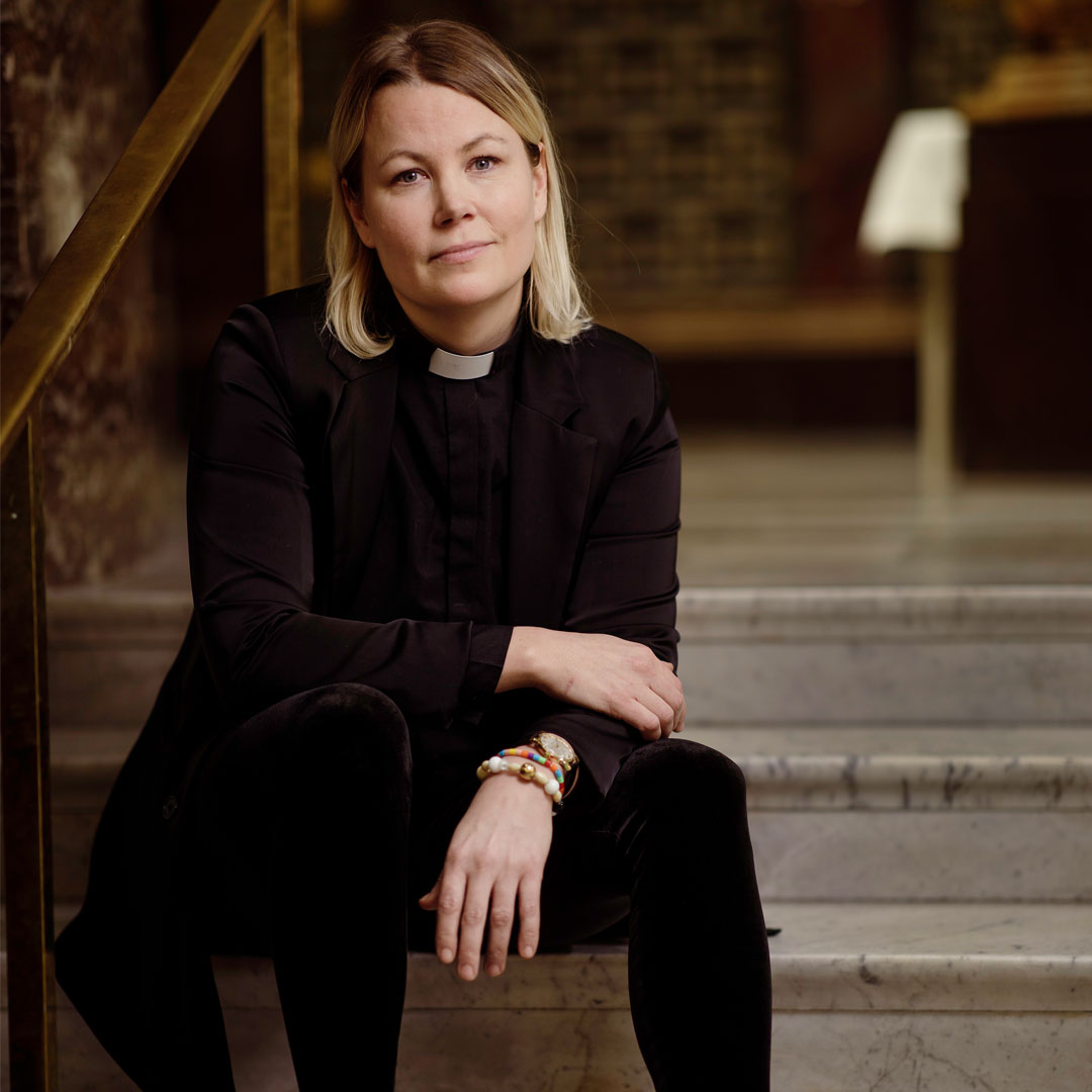 Kvinna i svart prästskjorta med frälsarkrans sitter i en stentrappa. | © Foto: Mikael M Johansson