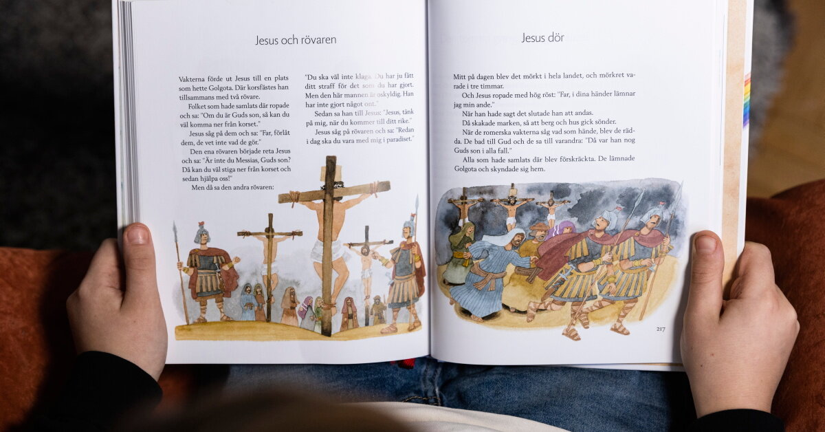 Barn läser ur barnens bibel, på uppslaget visas berättelsen om Jesus och rövaren samt när Jesus dör.