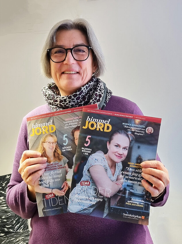 Leende kvinna med lila tröj och scarf håller upp två utgåvor av tidningen himmel och jord