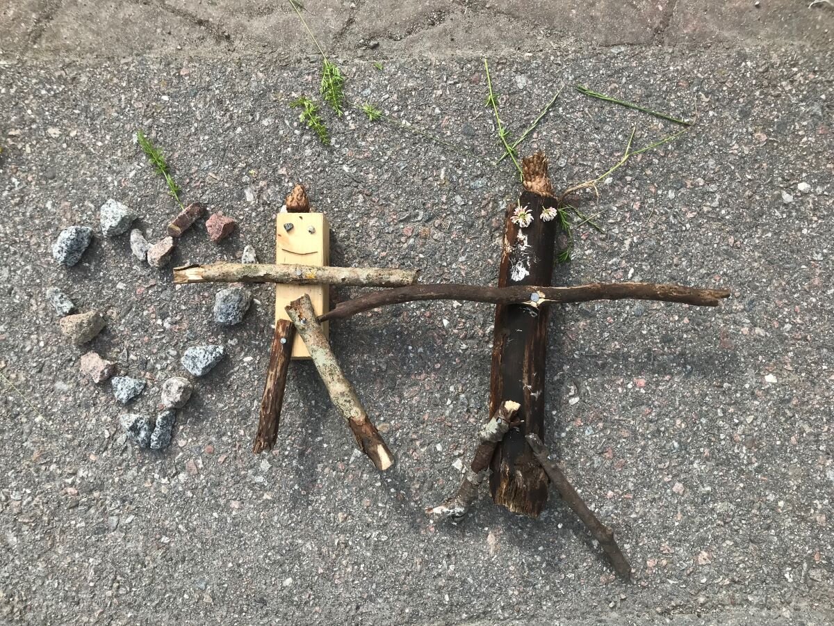 Två gubbar gjorda av träpinnar bredvid ett hjärta gjort av småsten.